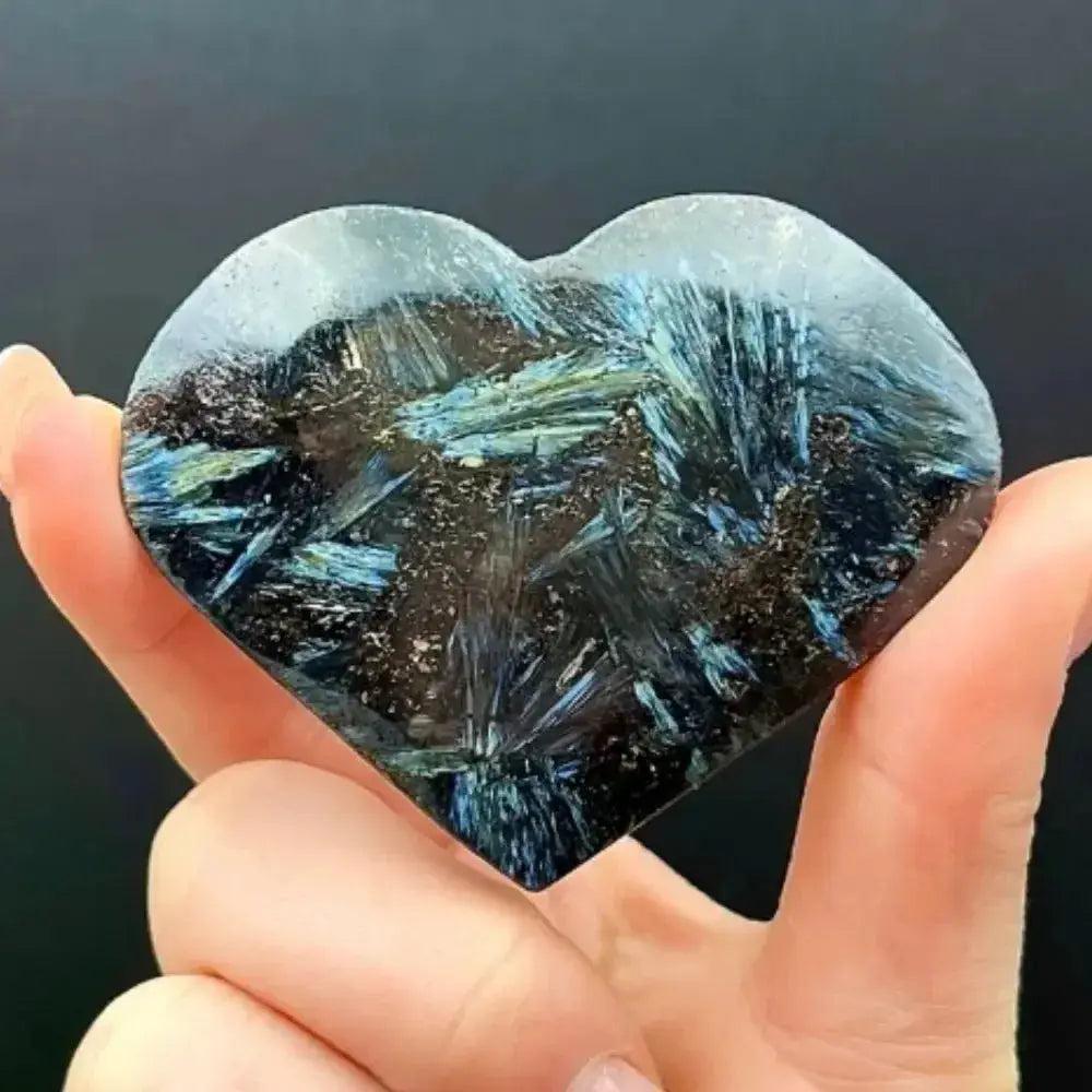 Hand holding a polished Astrophyllite Crystal Destiny heart with dark blue and black starburst inclusions.