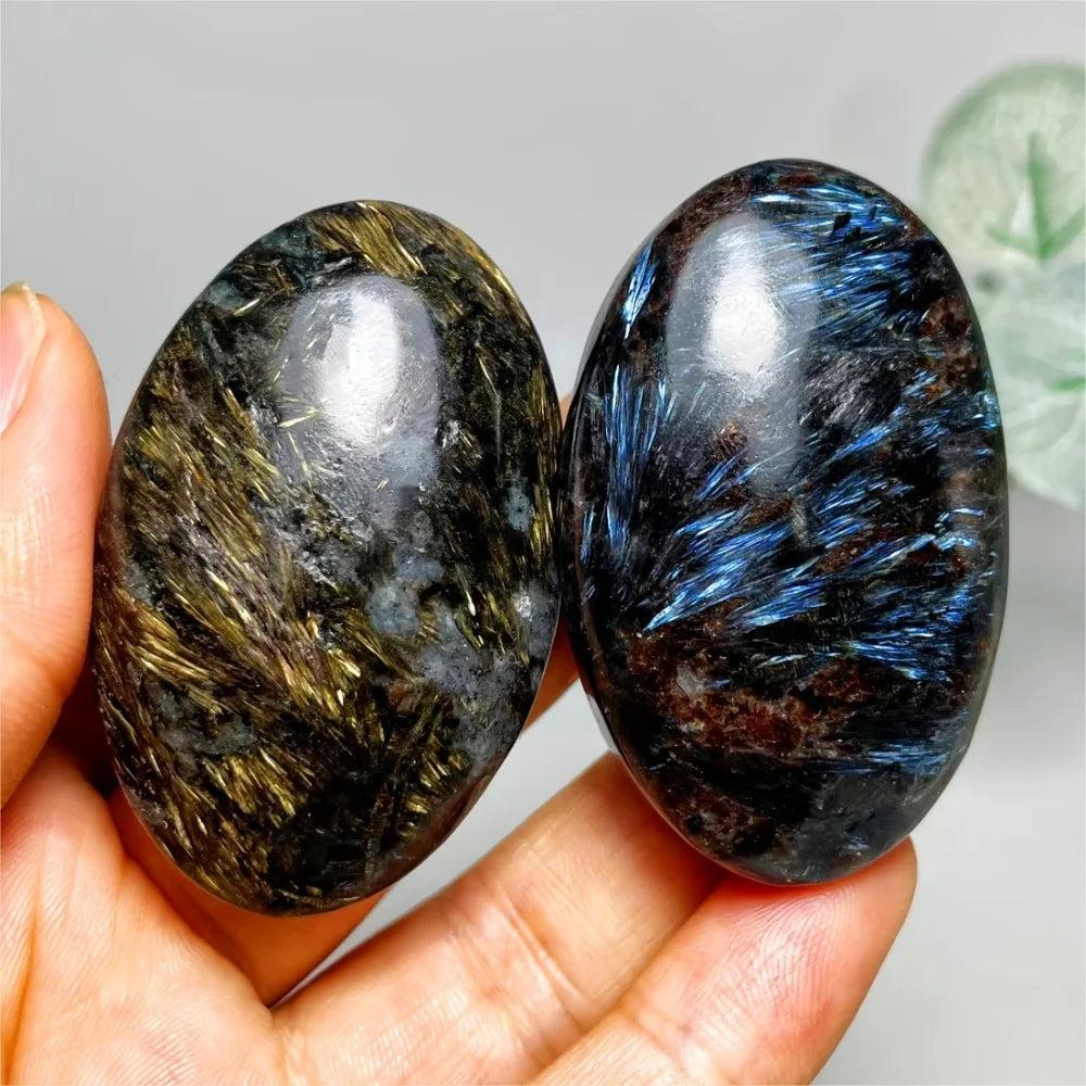 Polished Astrophyllite palm stones with shimmering gold and blue starburst inclusions for healing and energy balancing.