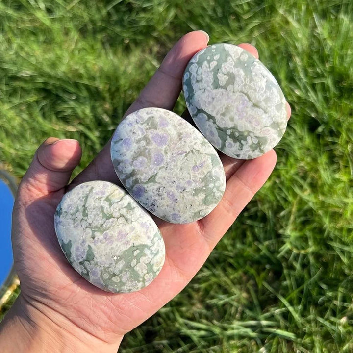 Three polished Atlantisite crystal palm stones with green and purple healing patterns held in a hand.