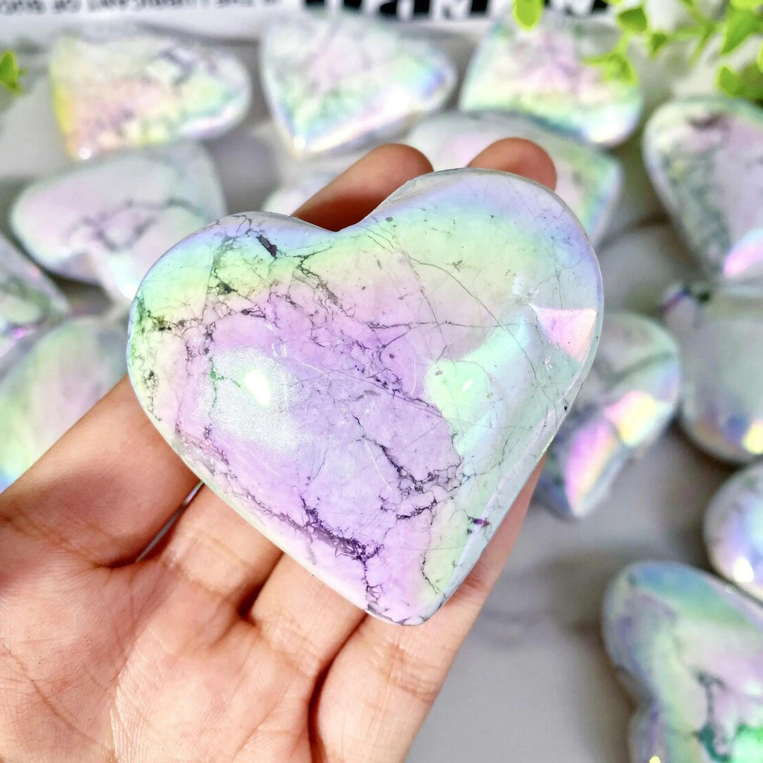 Hand holding a shimmering Aura Howlite crystal heart with iridescent rainbow hues, promoting tranquility from Crystal Destiny.