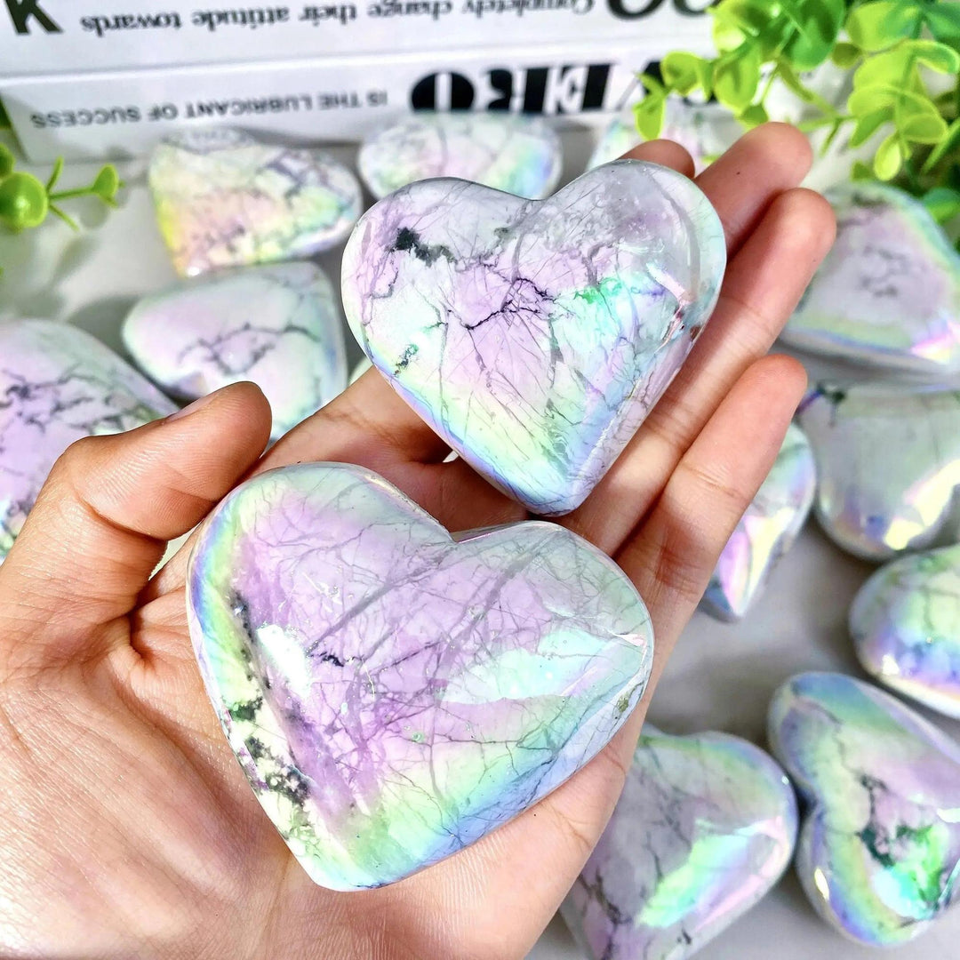 Two iridescent Aura Howlite crystal hearts held in a hand, showcasing rainbow hues and calming energy from Crystal Destiny.