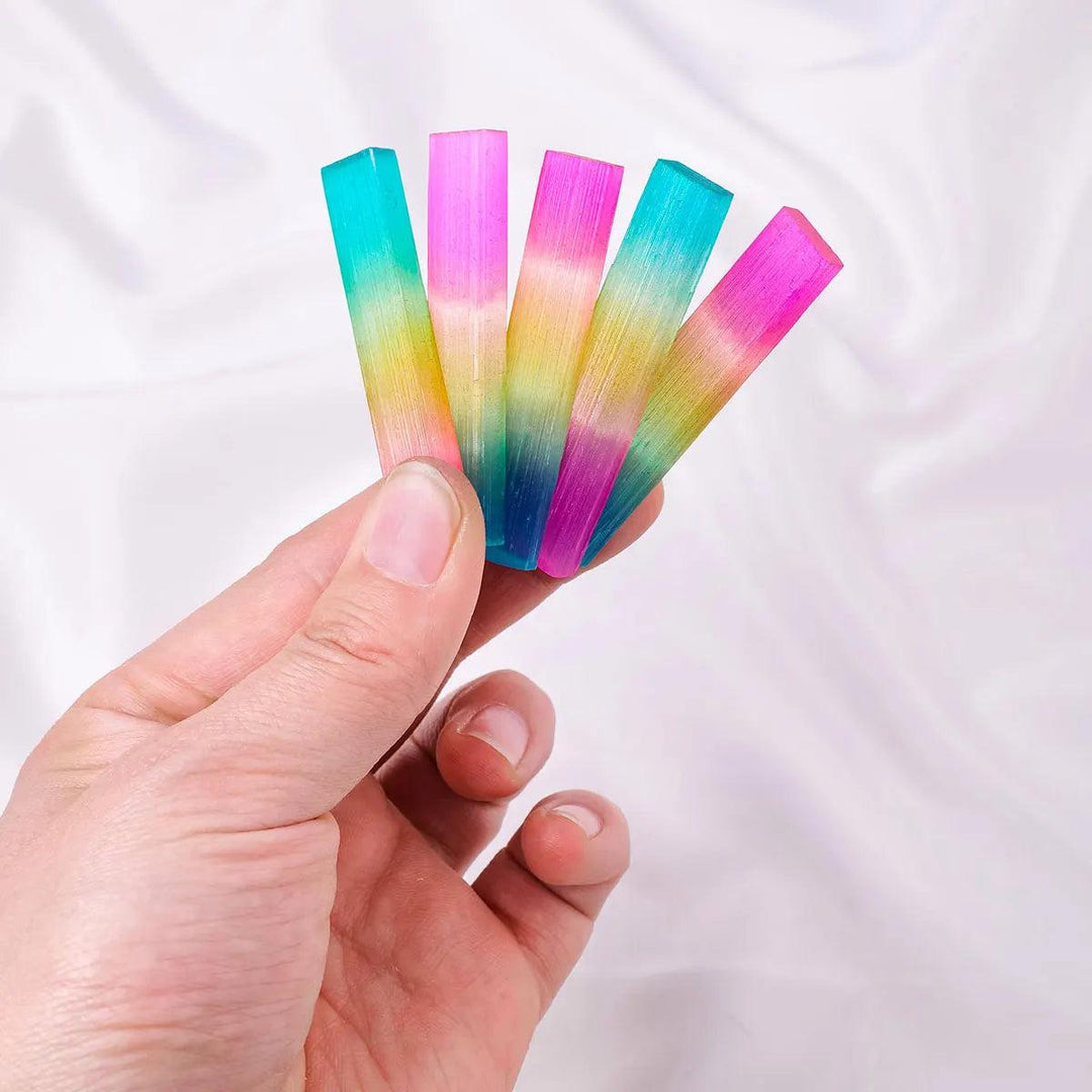 Hand holding Aura Selenite crystal sticks with a vibrant, iridescent rainbow metallic sheen for cleansing and healing.