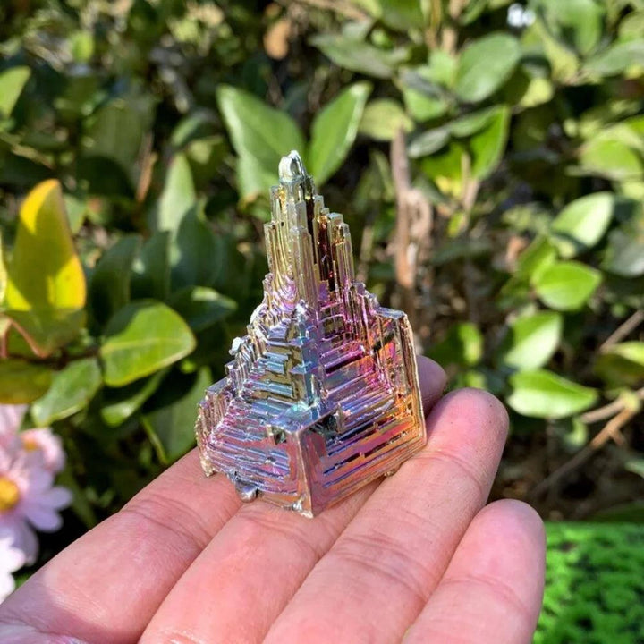 Iridescent Bismuth Crystal Pyramid for Manifestation, held in a hand against a green background.