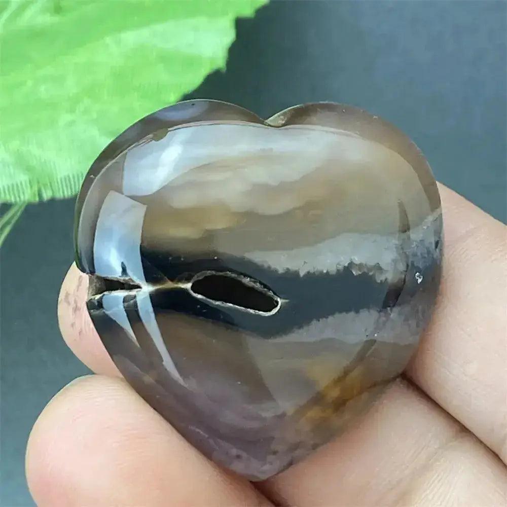 Polished black agate geode heart with a natural druzy crystal cavity, held in a hand.