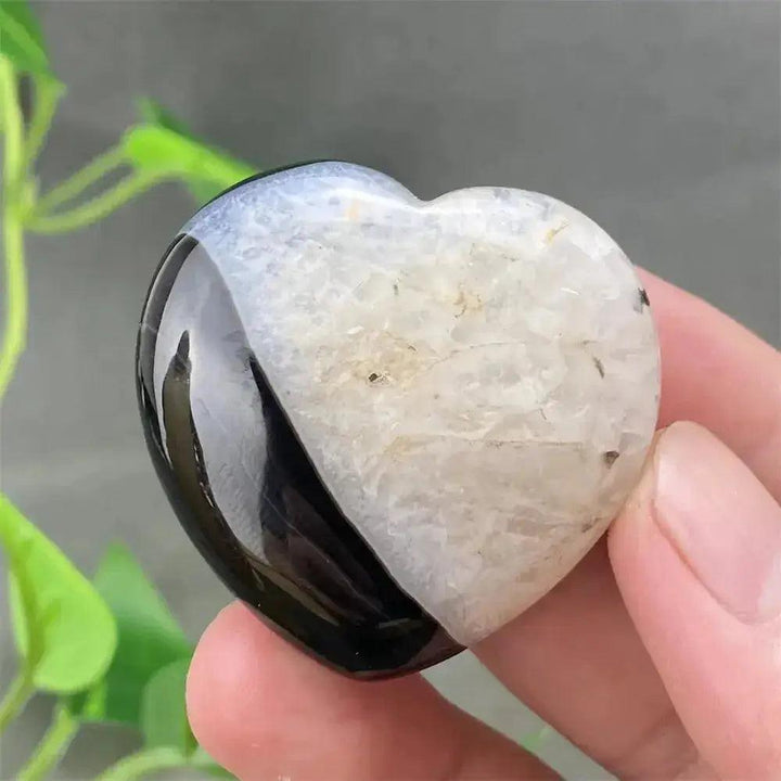 Hand holding a polished black and white agate geode heart with a sparkling druzy cave interior.