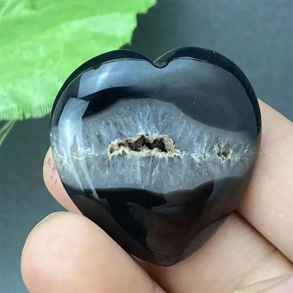 Polished black agate geode heart with a sparkling druzy crystal cave interior, held in a hand.