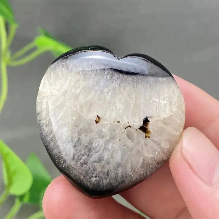 Hand holding a polished black agate geode heart with a sparkling white druzy crystal interior.