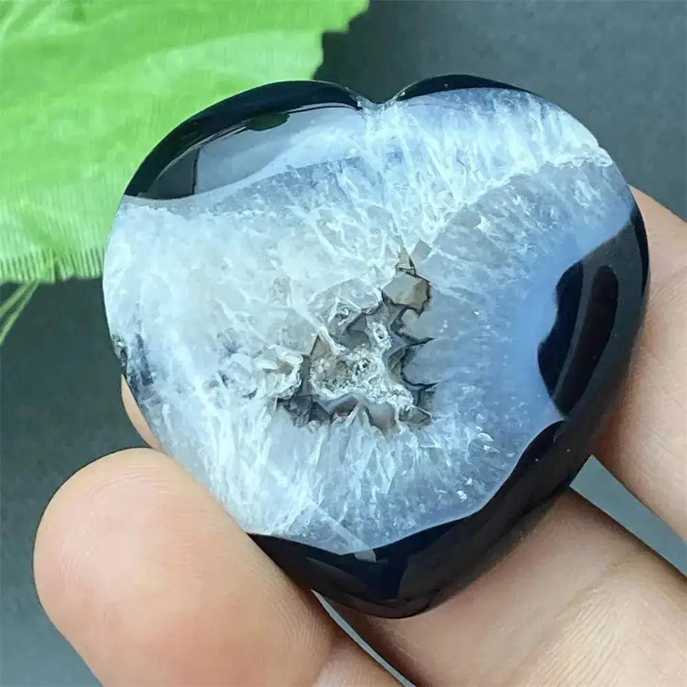 Polished black agate geode heart with a sparkling white druzy crystal cave interior, held in a hand.