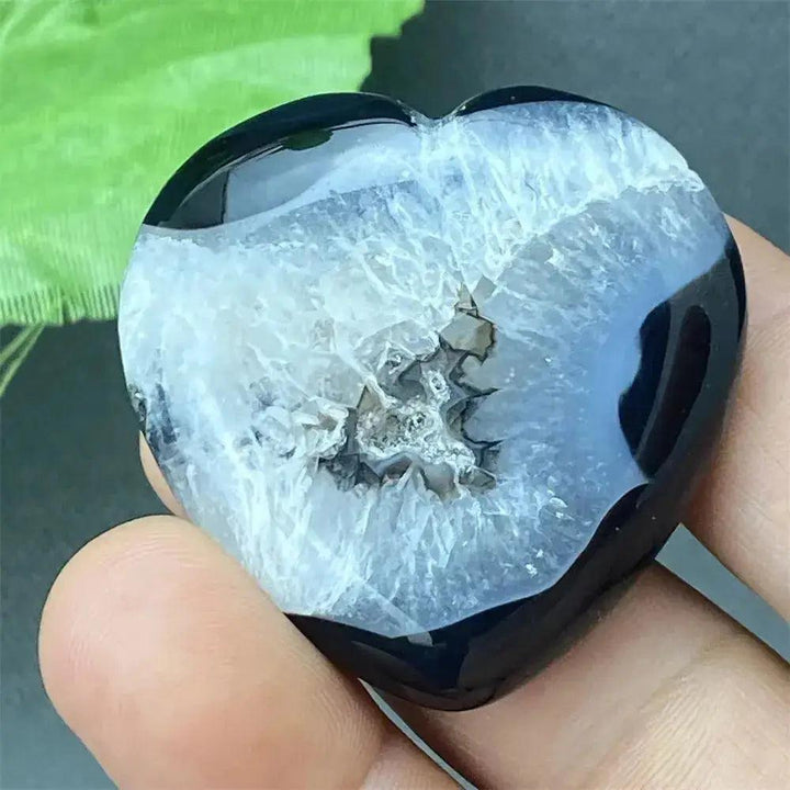Polished black agate geode heart with a sparkling white druzy crystal cave interior, held in a hand.