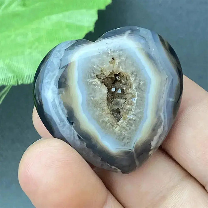 Polished black agate geode heart with a sparkling druzy crystal cave interior, held in a hand.