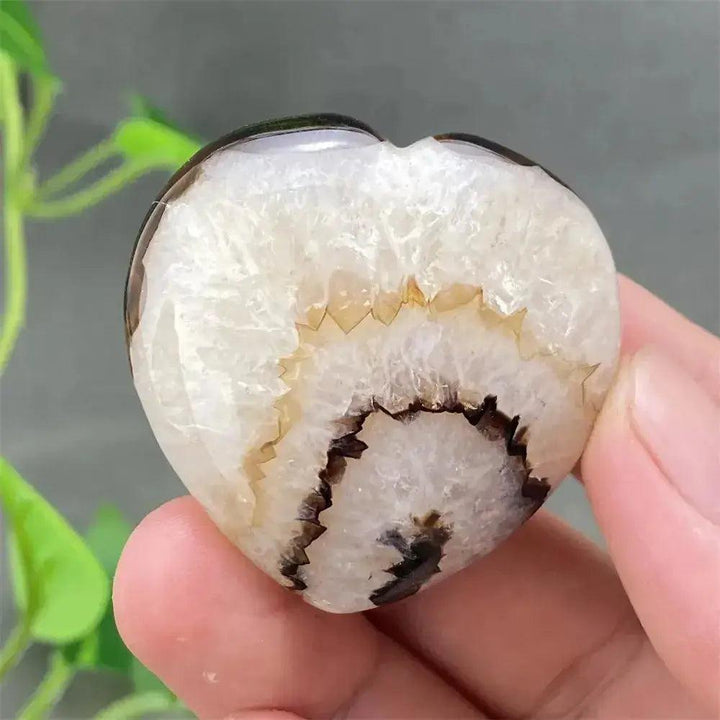 Black Agate geode heart with polished dark exterior and sparkling white druzy crystal interior, held in hand.