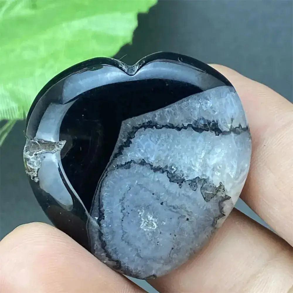 Polished black agate geode heart with a sparkling druzy crystal cavity, held in a hand.
