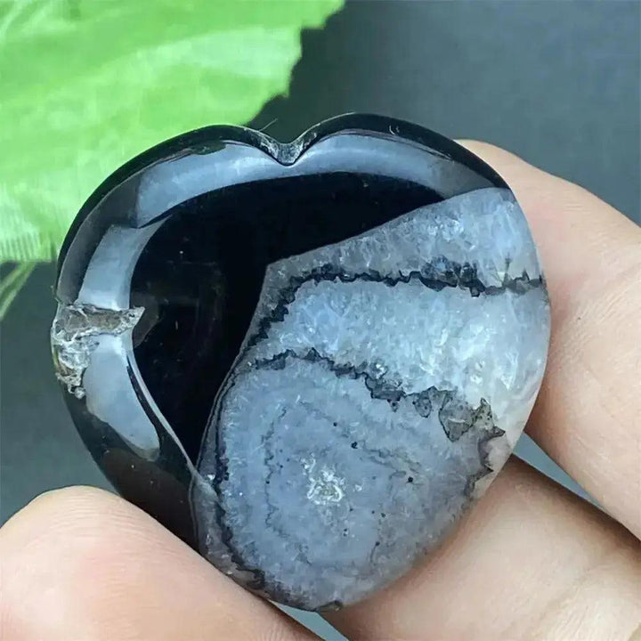 Polished black agate geode heart with a sparkling druzy crystal cavity, held in a hand.