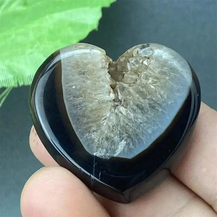 Polished black agate geode heart with a sparkling druzy crystal cave interior, held in a hand.