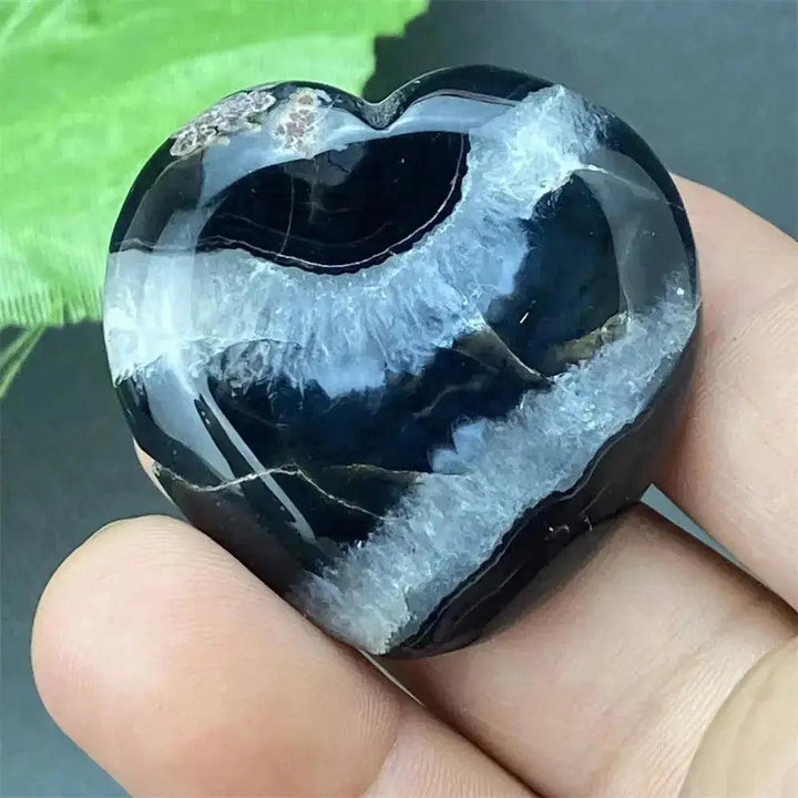 Polished black agate geode heart with a sparkling white druzy crystal cave interior, held in a hand.