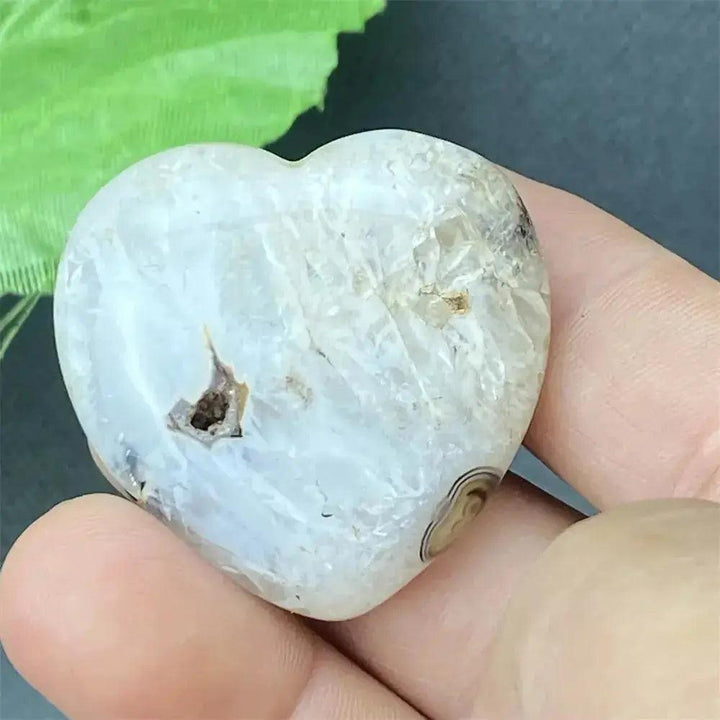 Polished white agate geode heart with natural druzy crystals, held in a hand.