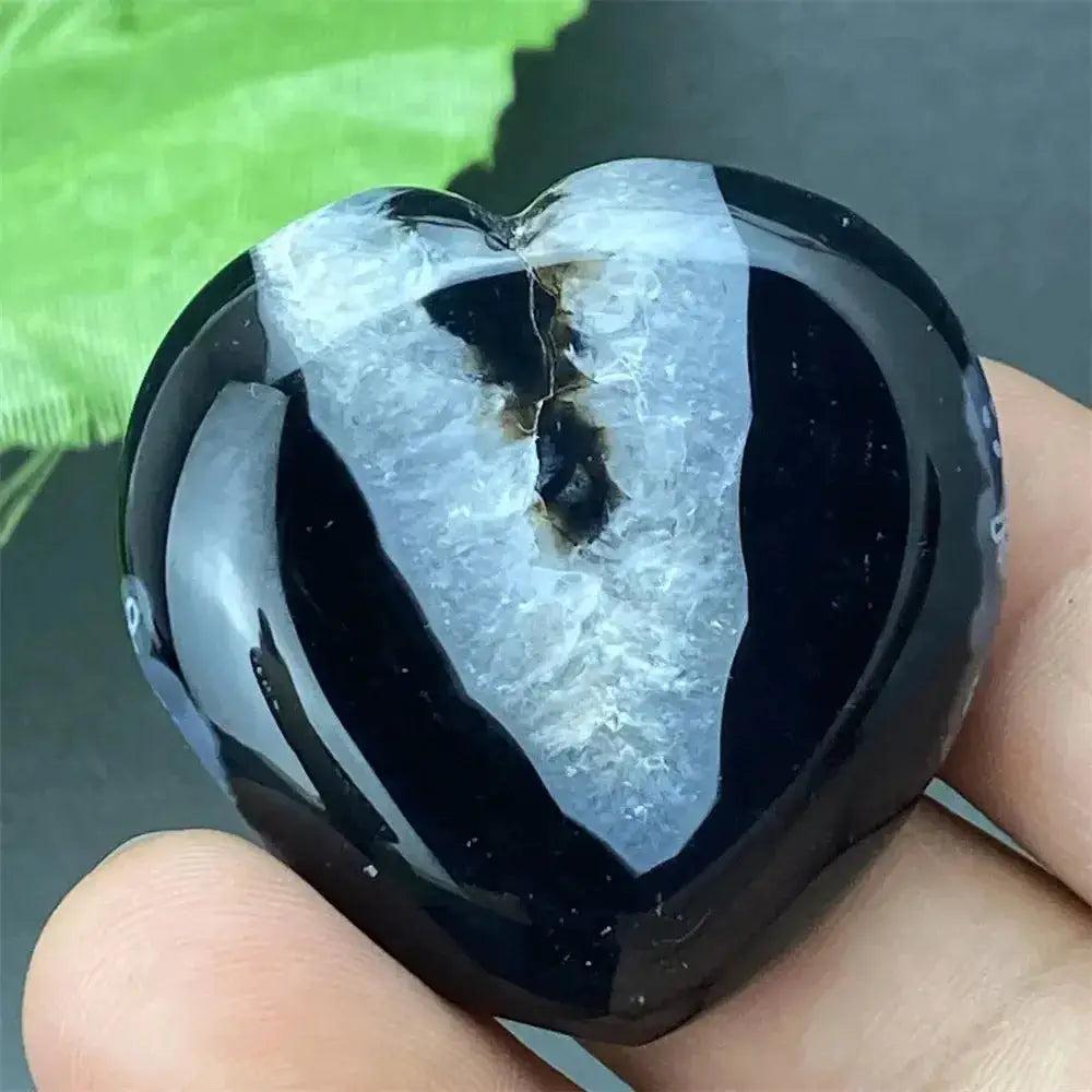 Polished black agate geode heart with a sparkling white druzy crystal cave interior, held in a hand.