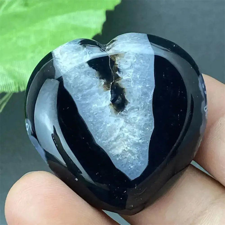 Polished black agate geode heart with a sparkling white druzy crystal cave interior, held in a hand.