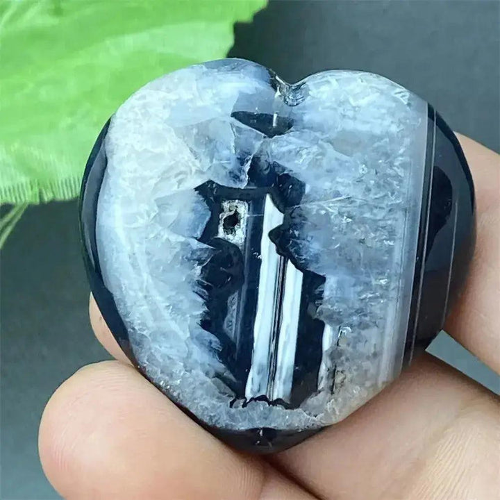 Polished black agate geode heart with a sparkling white and grey druzy crystal cave interior, held in a hand.