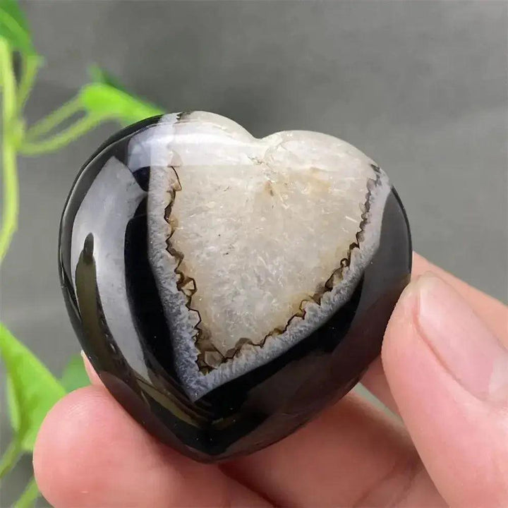 Polished black agate geode heart with a sparkling white druzy crystal cave interior, held in a hand.