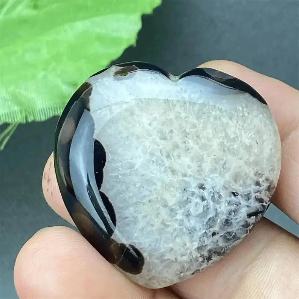 Polished black agate geode heart with a sparkling white druzy crystal interior, held in a hand.