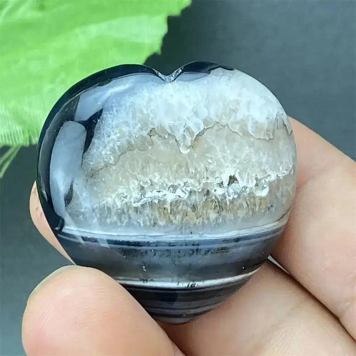 Polished black agate geode heart with a sparkling white druzy crystal interior, held in a hand.