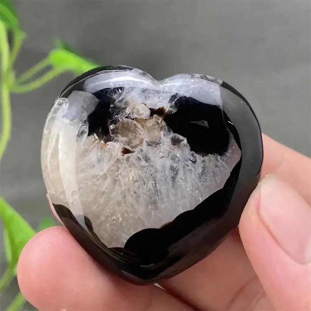 Polished black agate geode heart with a sparkling white druzy crystal cave interior, held in a hand.