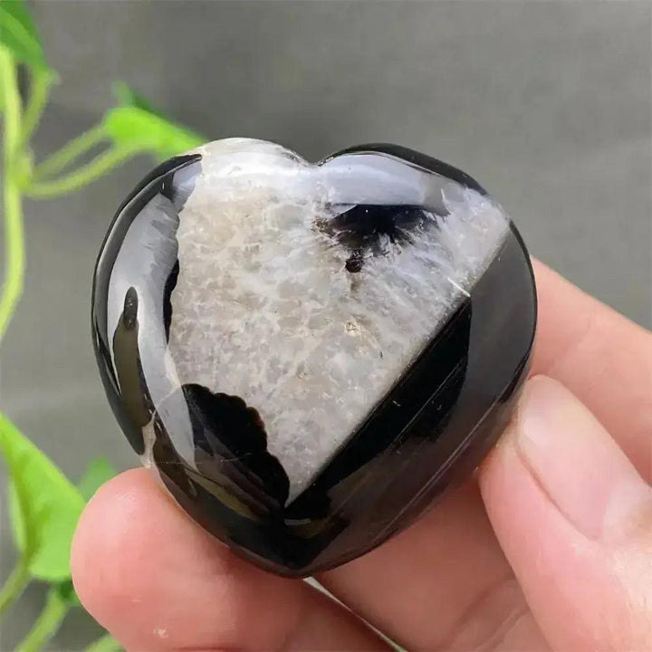 Polished black agate geode heart with a sparkling white druzy crystal cave interior, held in a hand.