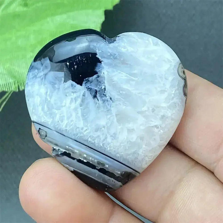 Black Agate geode heart with a polished dark exterior and sparkling white druzy crystal interior, held in a hand.