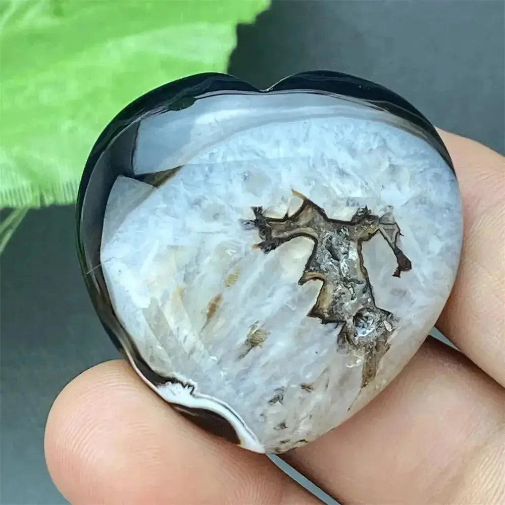 Polished black agate geode heart with a sparkling white druzy crystal cave interior, held in a hand.