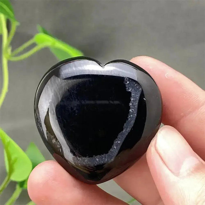 Polished black agate geode heart with a sparkling druzy crystal cavity, held in a hand.
