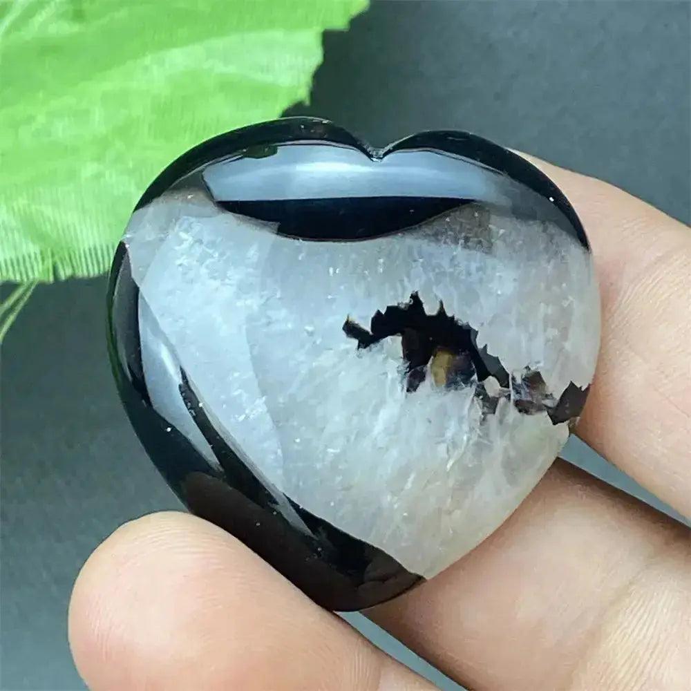 Polished black agate geode heart with a sparkling white druzy crystal cave interior, held in a hand.