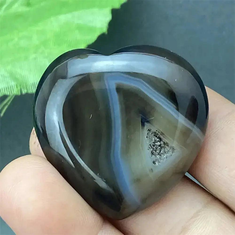 Polished black agate geode heart with natural druzy crystal cavity, held in a hand.