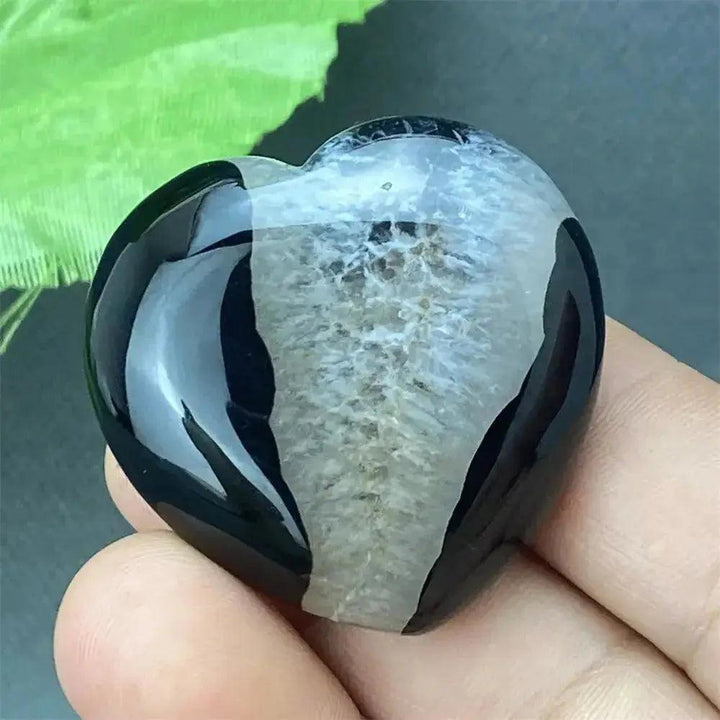 Polished black agate geode heart with a sparkling white druzy crystal interior, held in a hand.
