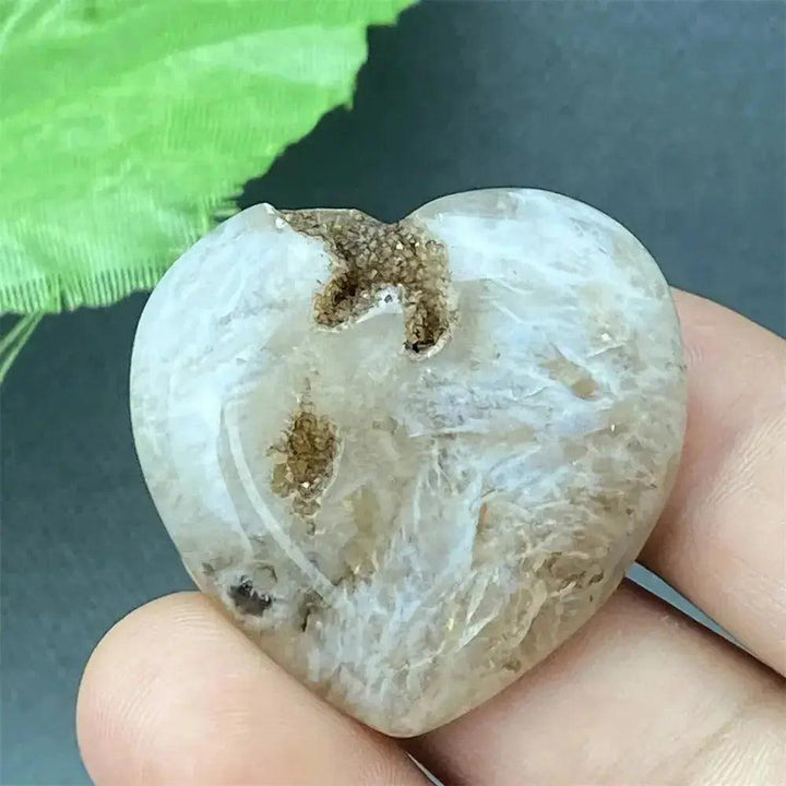Polished white agate geode heart with a natural druzy crystal cavity, held in a hand.