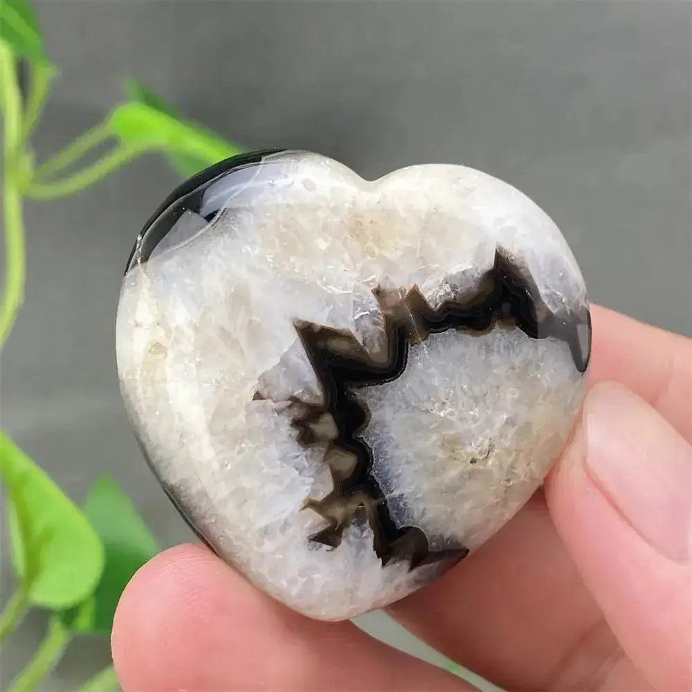 Polished black agate heart with natural white and black druzy crystal patterns, held in a hand.