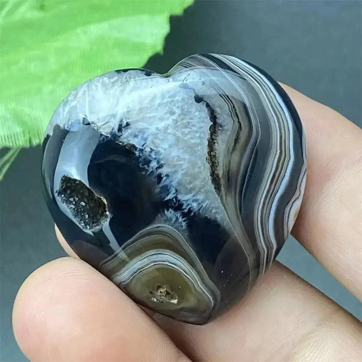 Polished black agate geode heart with a sparkling white druzy crystal cave interior, held in a hand.