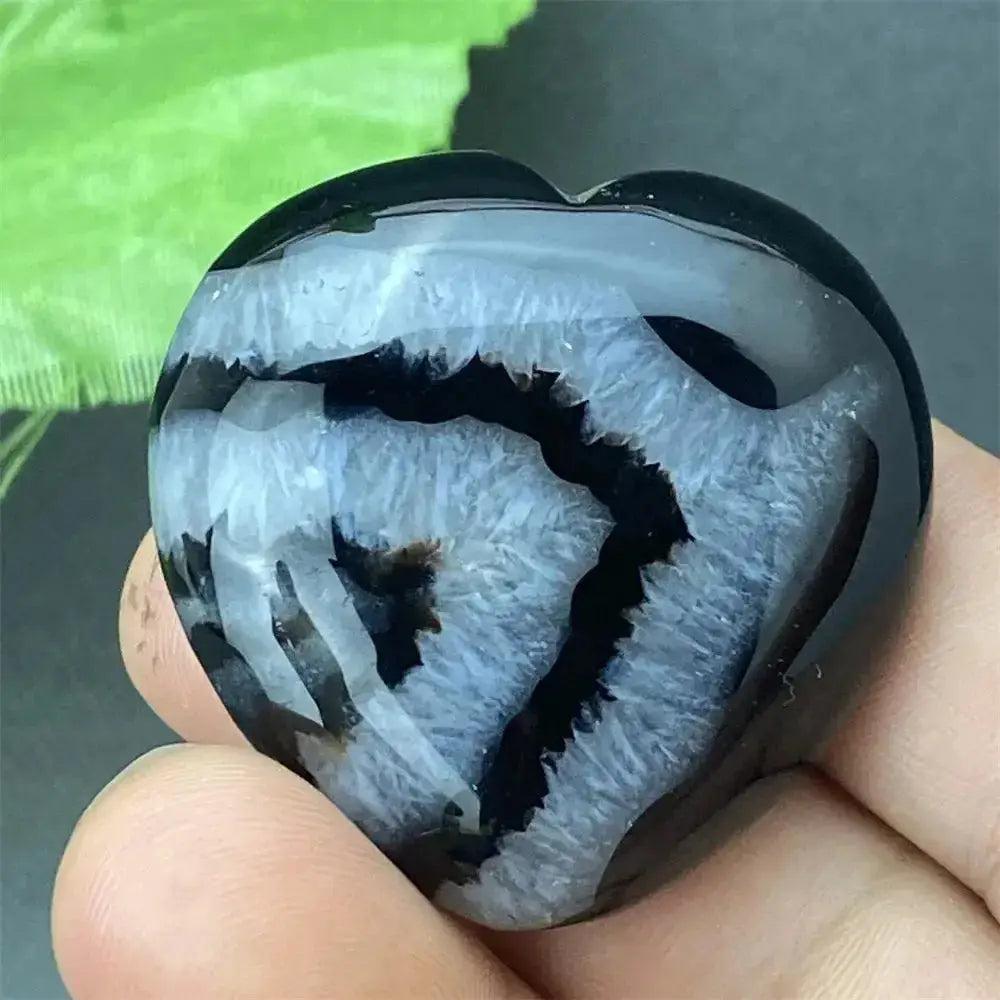 Polished black agate geode heart with a sparkling white druzy crystal cavity, held in a hand.