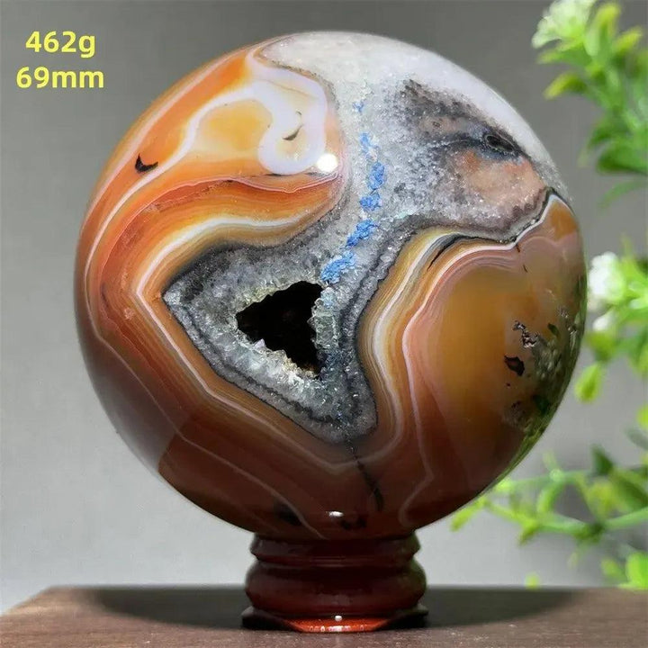 Polished Agate sphere with vibrant orange, white, and gray bands, featuring a sparkling geode cavity.