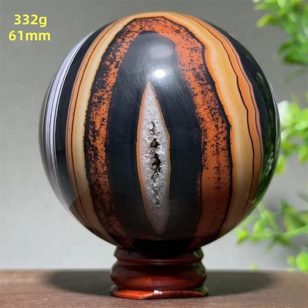 Polished Black Banded Agate sphere with dramatic black, orange, and white striations, on a wooden stand.