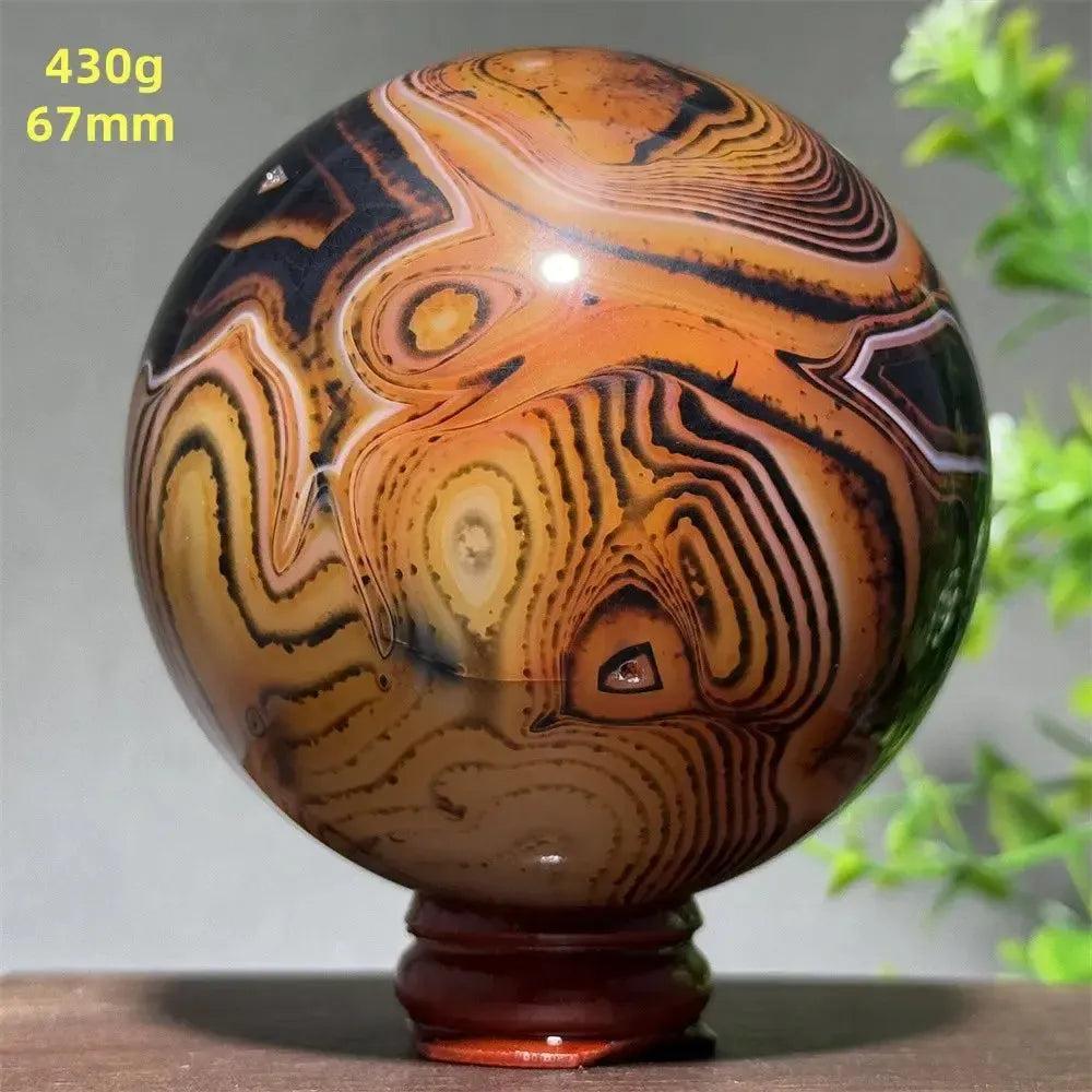 Polished Black Banded Agate Sphere with dramatic black, orange, and white striations on a wooden stand.