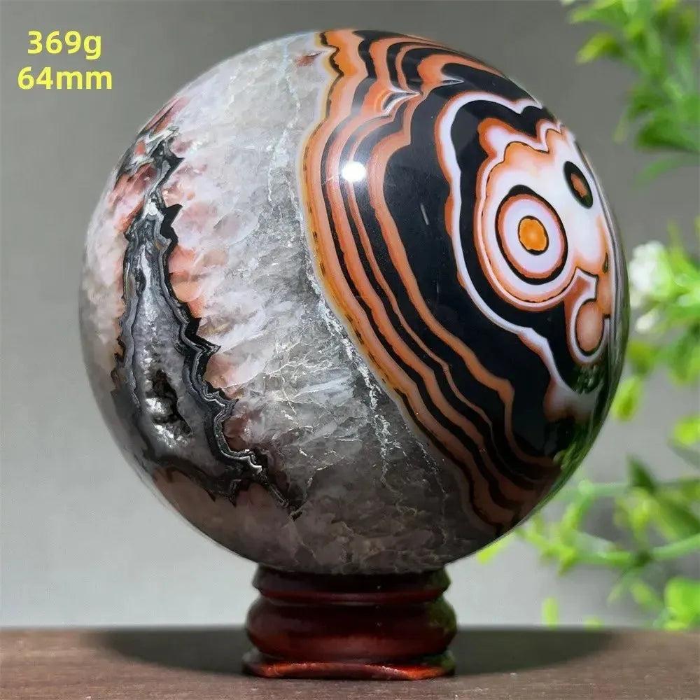 Polished Black Banded Agate sphere with dramatic black, orange, and white striations on a wooden stand.