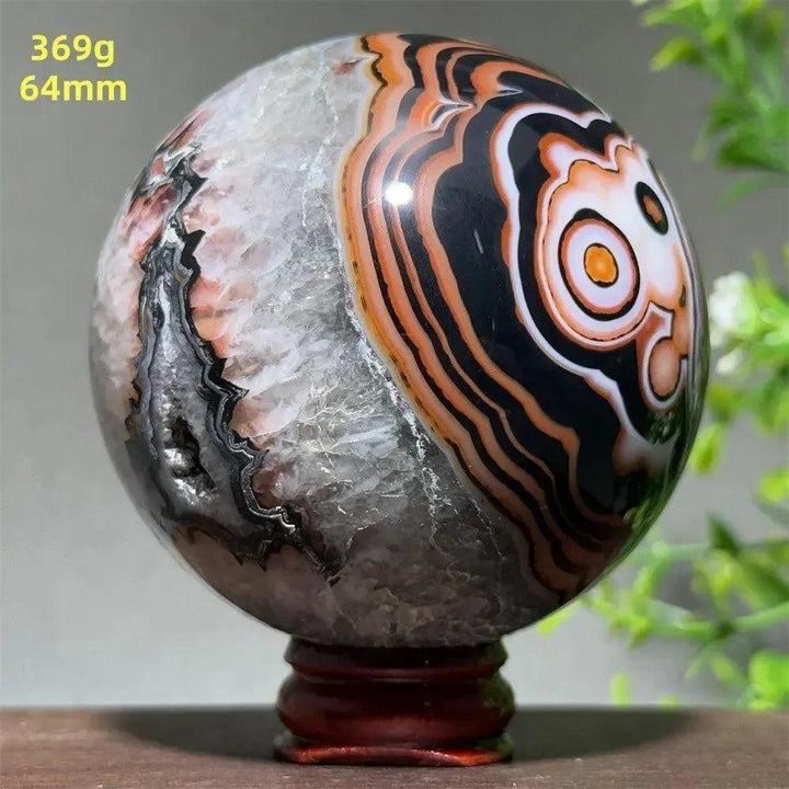 Polished Black Banded Agate sphere with dramatic black, orange, and white striations on a wooden stand.