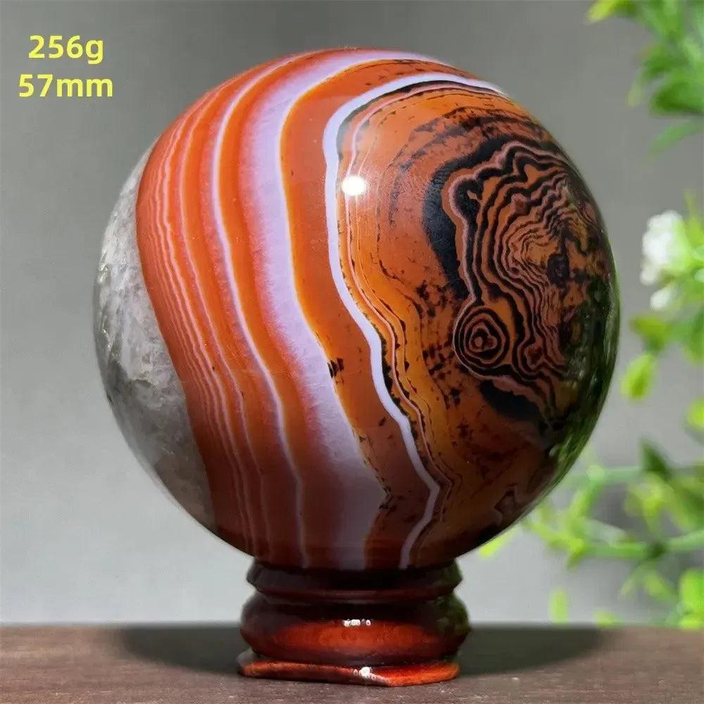 Polished Black Banded Agate sphere with dramatic black, charcoal, and white striations on a wooden stand.