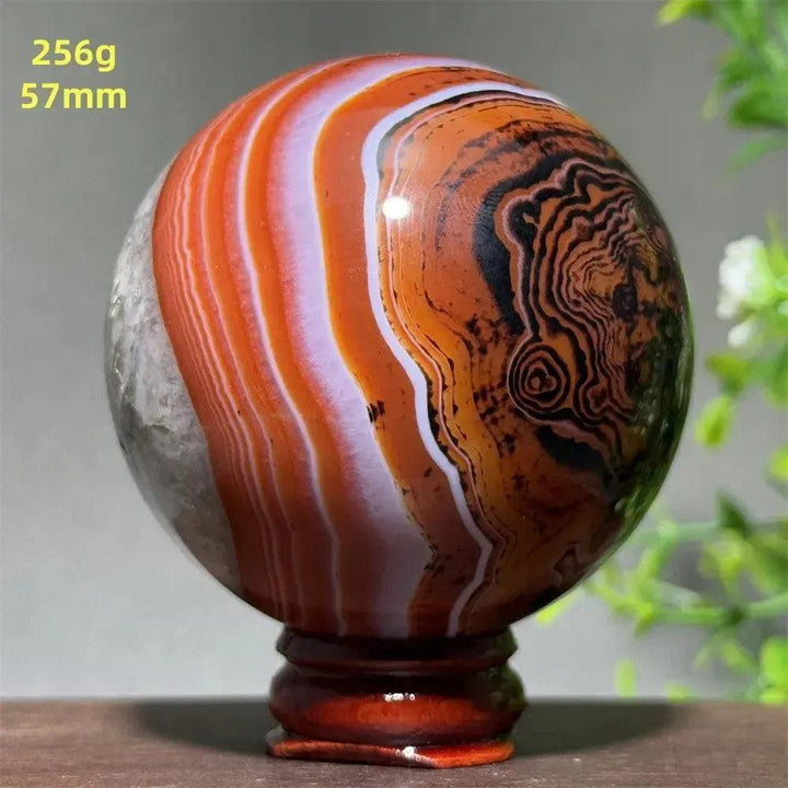 Polished Black Banded Agate sphere with dramatic black, charcoal, and white striations on a wooden stand.