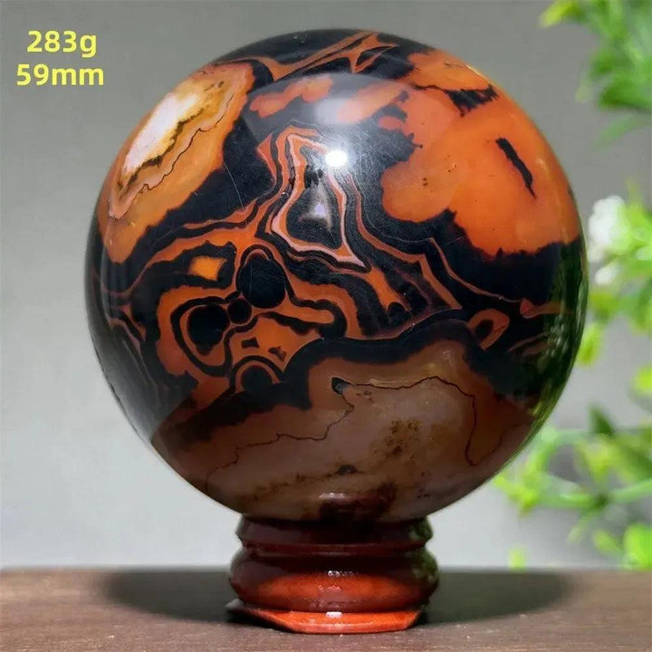 Polished Black Banded Agate sphere with striking black, orange, and brown striations, on a wooden stand.