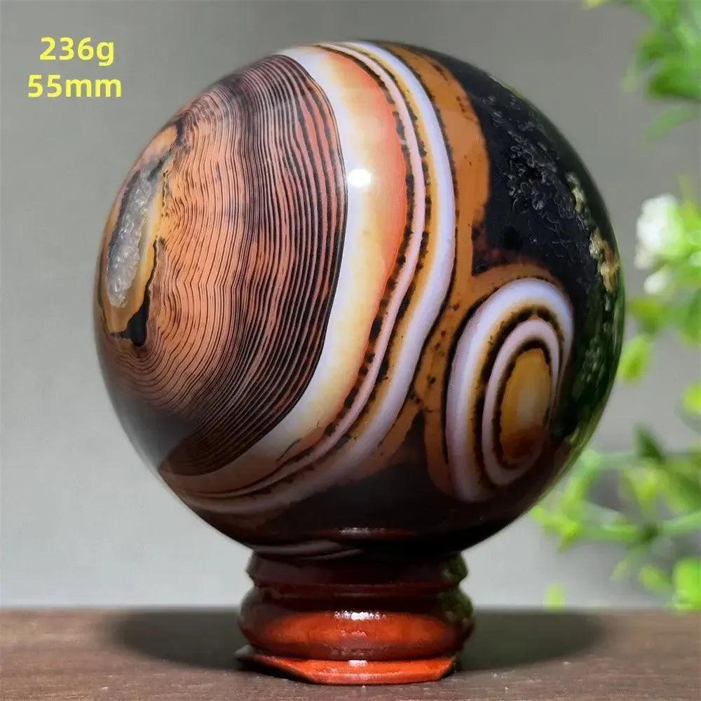 Polished Black Banded Agate Sphere with dramatic black, charcoal, white, and orange striations on a wooden stand.