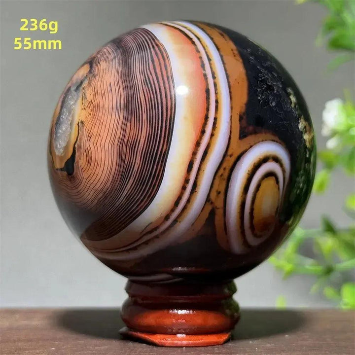 Polished Black Banded Agate Sphere with dramatic black, charcoal, white, and orange striations on a wooden stand.