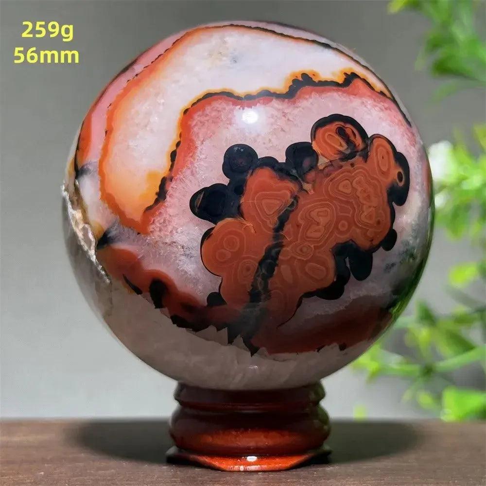 Polished Black Banded Agate sphere with dramatic black and charcoal striations on a wooden stand.