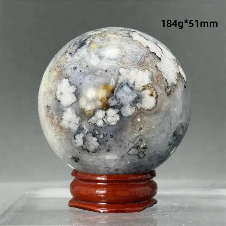 Black Cherry Blossom Agate Sphere with dramatic dark and light floral banding on a red wooden stand.